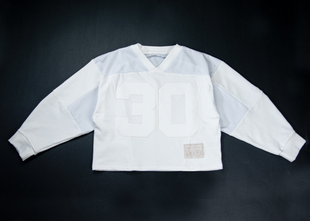 A vintage white long-sleeve football jersey with the number 30 in white on the front, laid flat against a dark background.