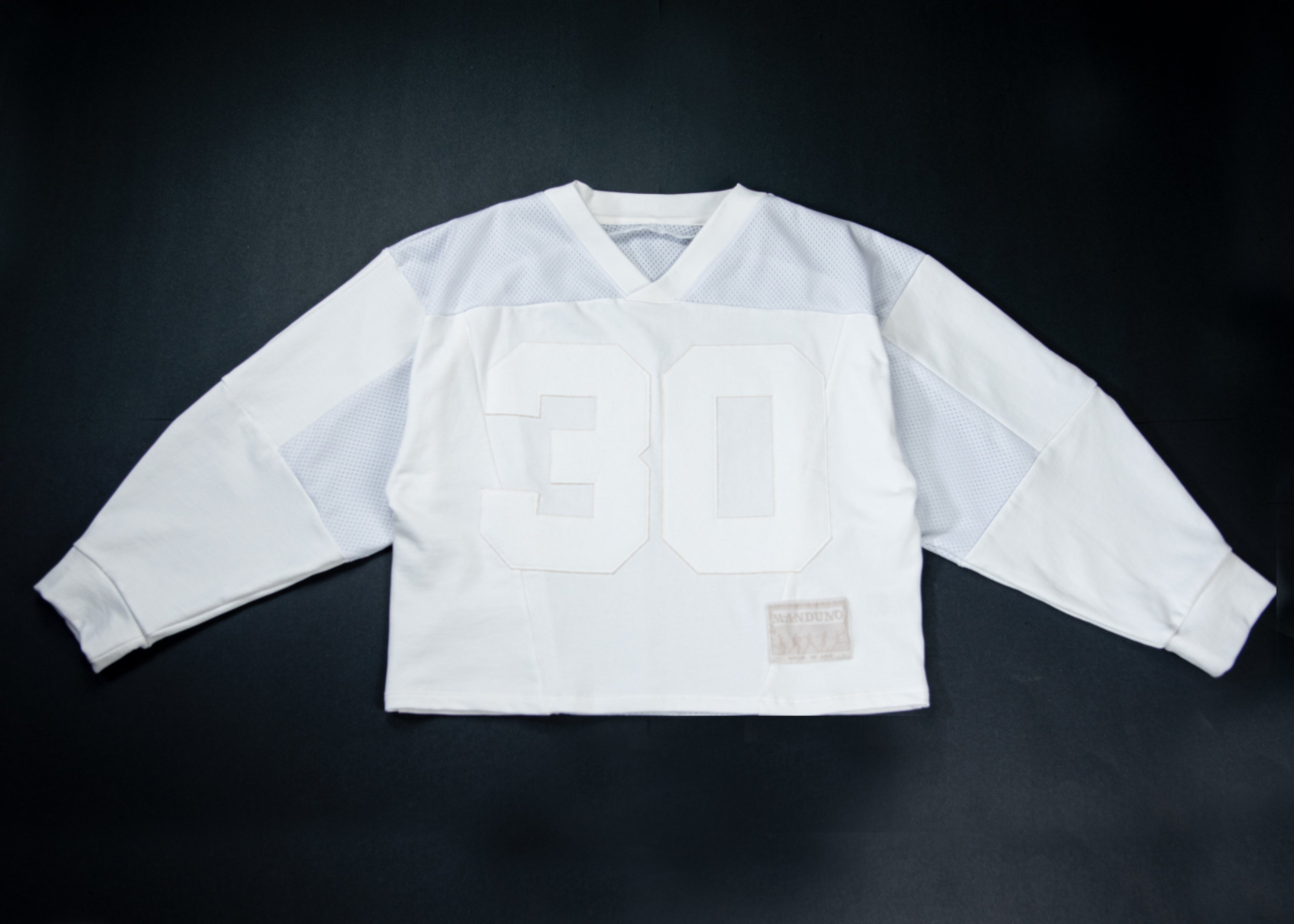 A vintage white long-sleeve football jersey with the number 30 in white on the front, laid flat against a dark background.