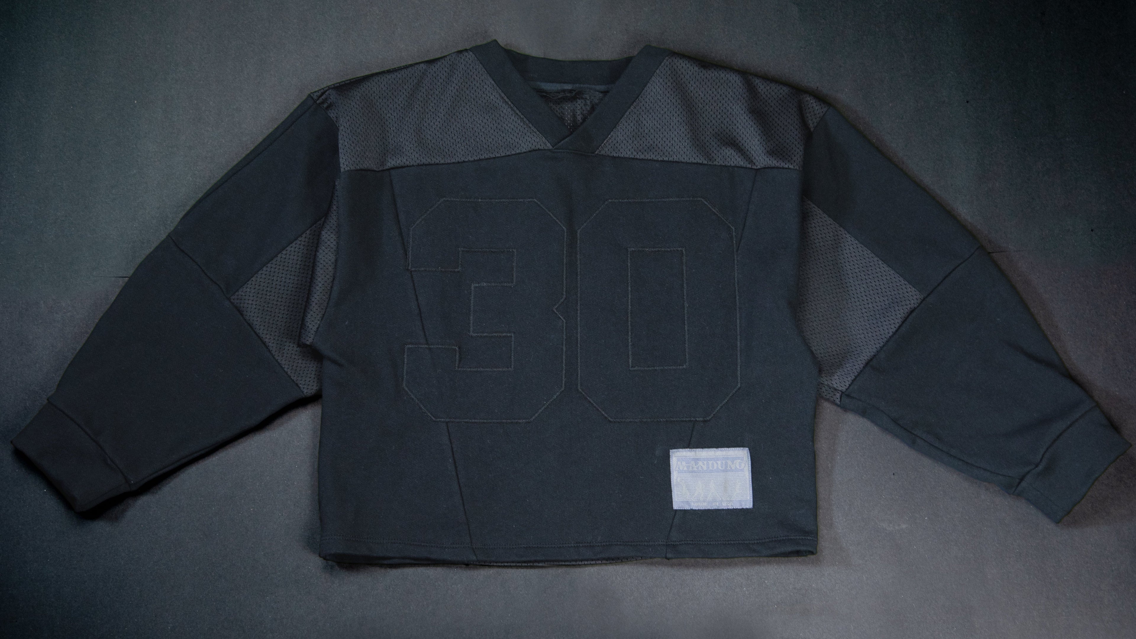 A black vintage football jersey with '30' stitched on the front, laid flat on a dark gray background.