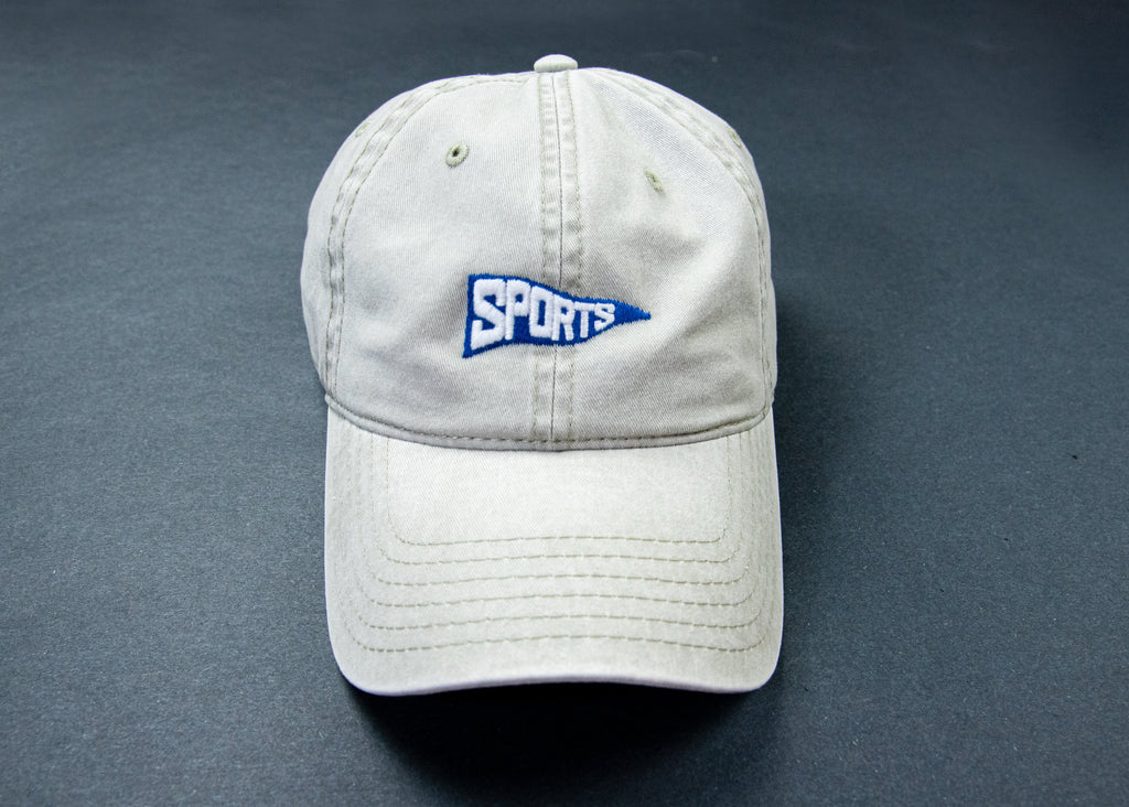 A light beige baseball cap with a blue and white embroidered 'SPORTS' pennant logo on the front, displayed on a dark gray background.
