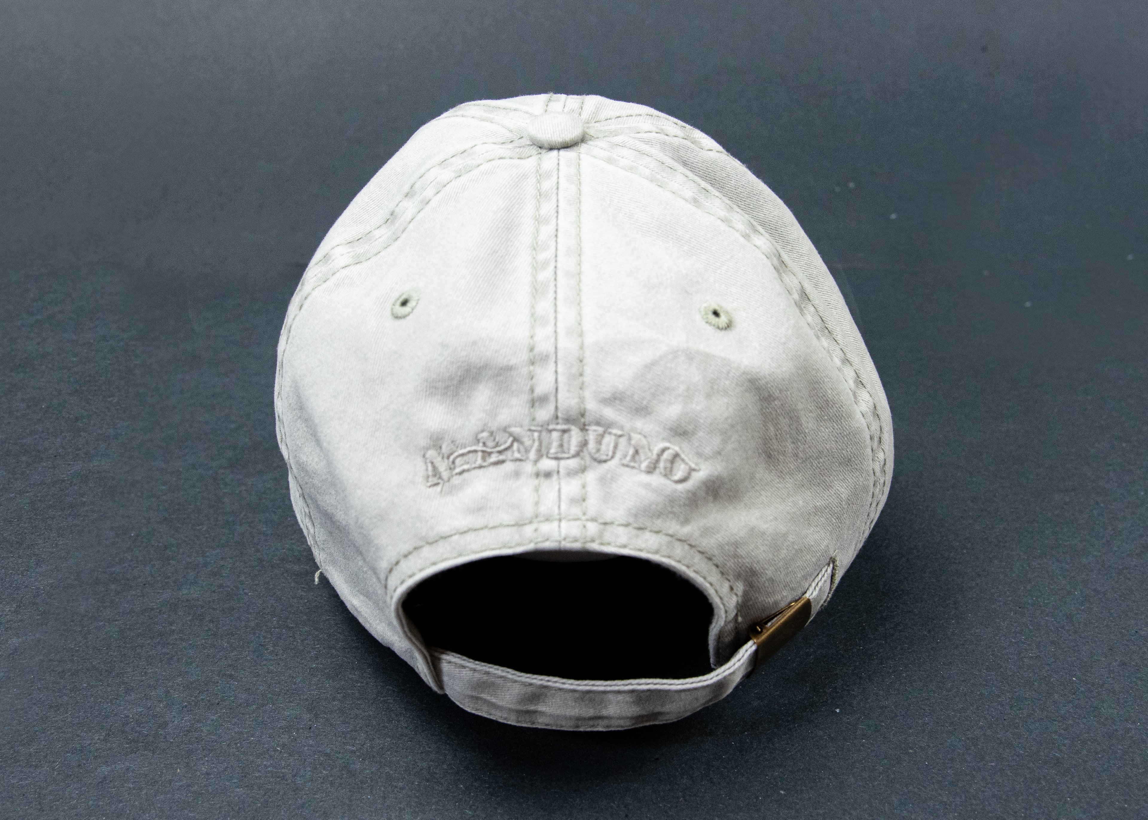 A light beige or off-white baseball cap shown from the back, featuring a distressed texture and tonal embroidered logo on the back panel, set against a dark gray background.